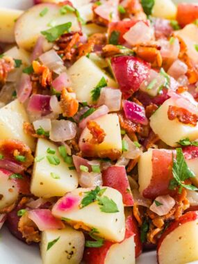 Close up of hot German potato salad with bacon in a white bowl.