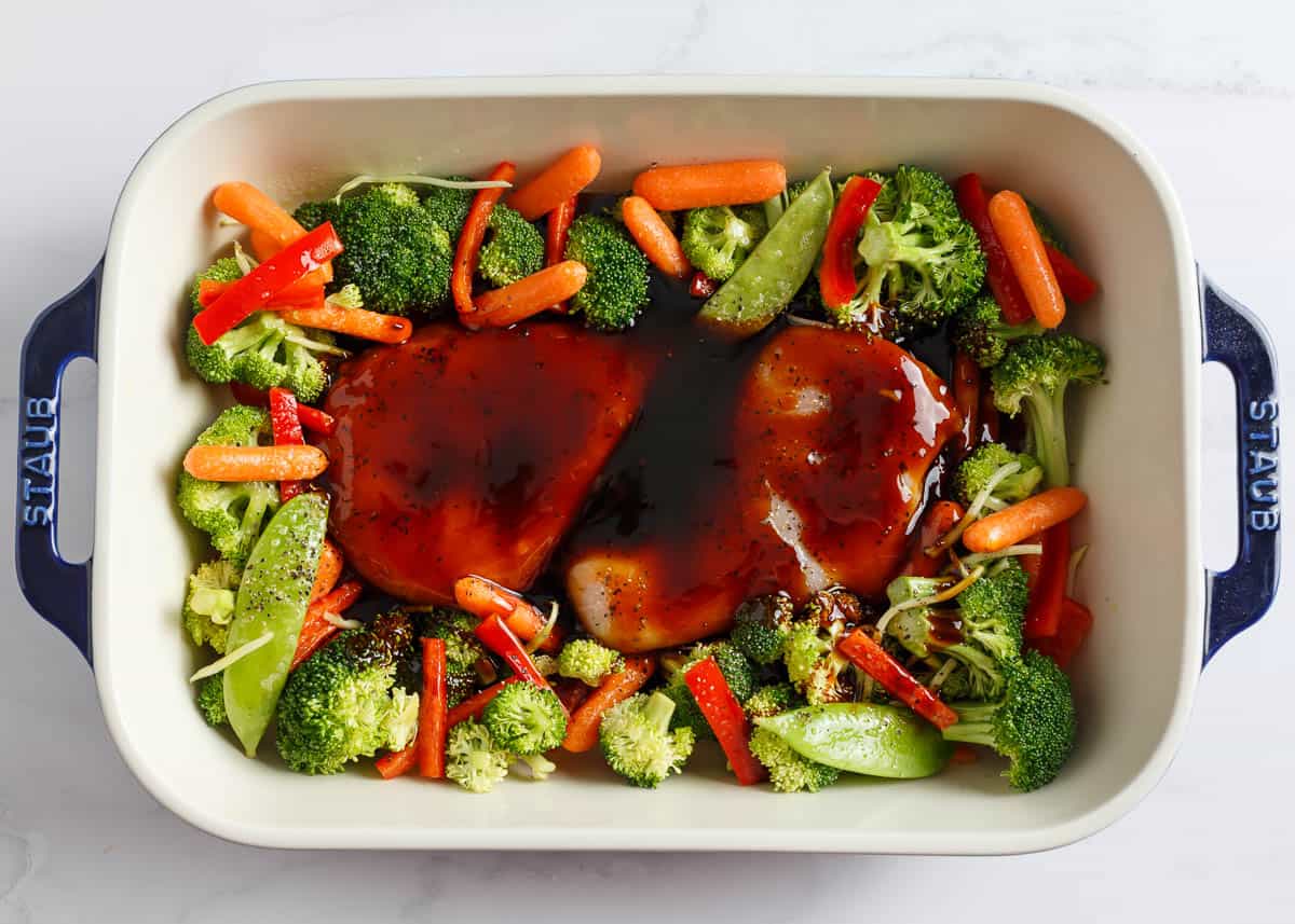 All you need for this easy chicken teriyaki casserole is chicken, cooked rice, veggies, and teriyaki sauce for a quick, healthy, and flavorful meal any night of the week! Vegetables with whole chicken pieces in a white baking dish with teriyaki sauce.