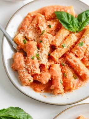 Pink sauce pasta in a large bowl with basil and Parmesan garnish.