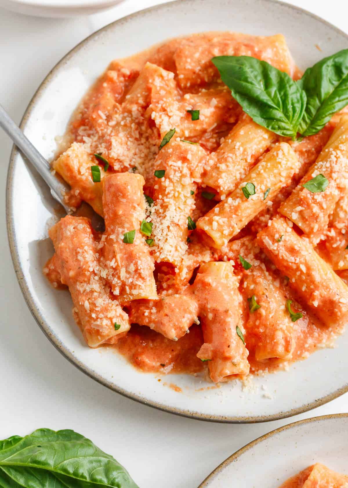 Pink sauce pasta in a large bowl with basil and Parmesan garnish.