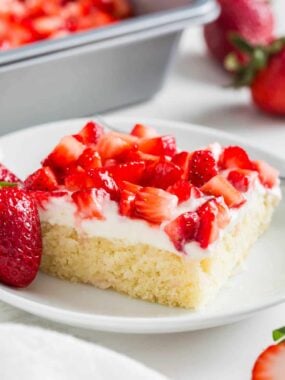Strawberry shortcake bar on a plate topped with cream cheese frosting and fresh strawberries.