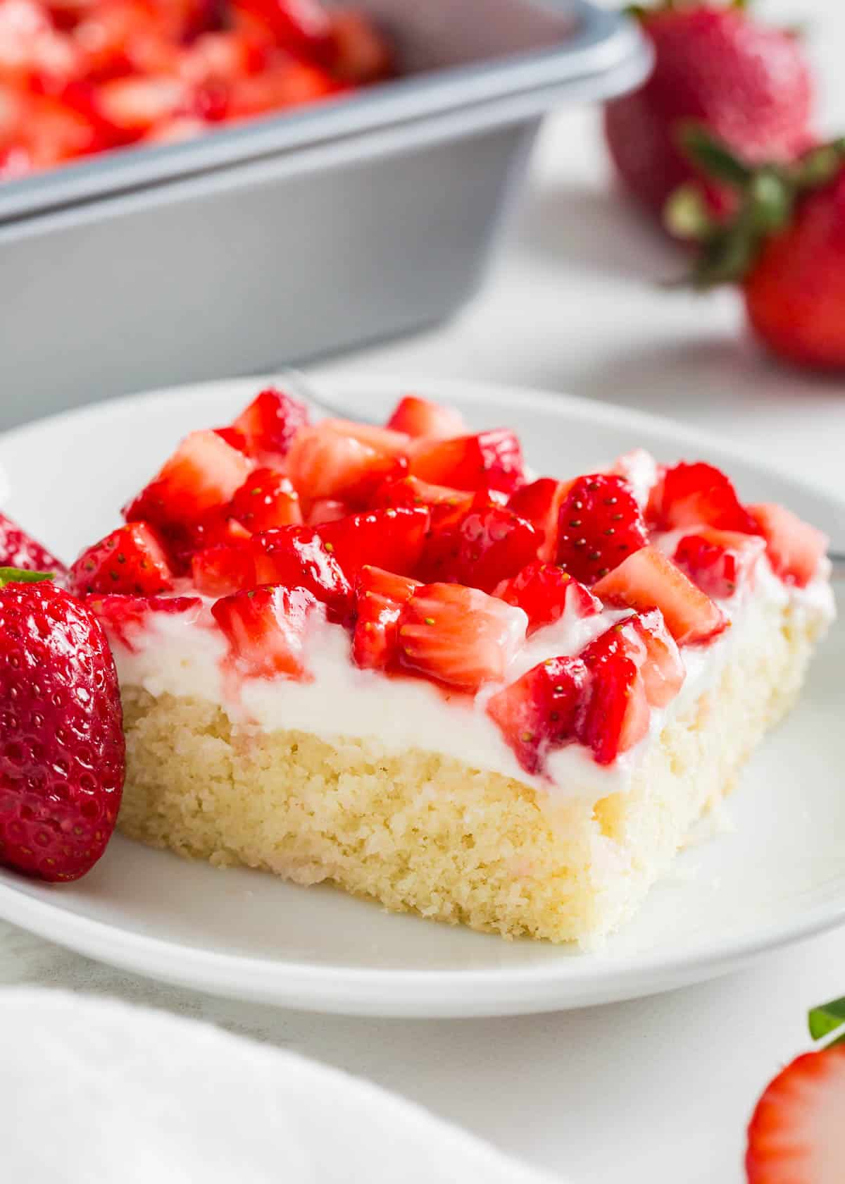 Made with a thin vanilla cake, cream cheese frosting, and sweet strawberries, these strawberry shortcake bars are a sheet cake version of the classic layered cake! Strawberry shortcake bars on a plate.