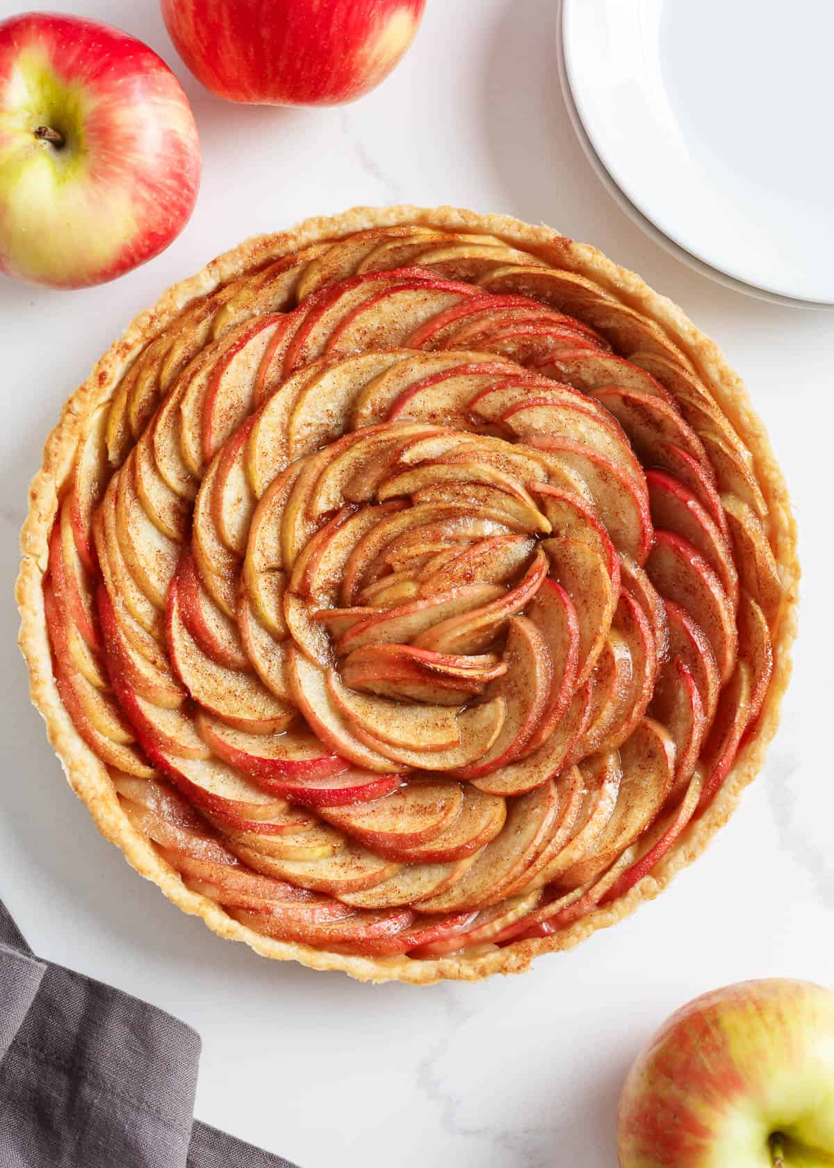 Tender, crisp apple slices nestled in a flaky crust, brushed with lemon juice, cinnamon, vanilla, and brown sugar, results in a French apple tart that is almost too pretty to eat! Apple tart on counter.