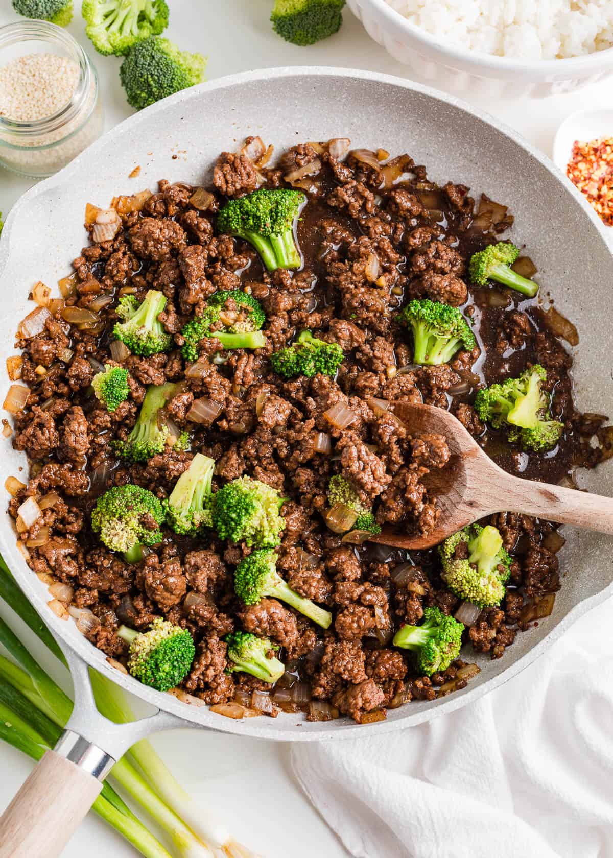 Cooking ground beef and broccoli in a skillet with white rice in a bowl on the side.