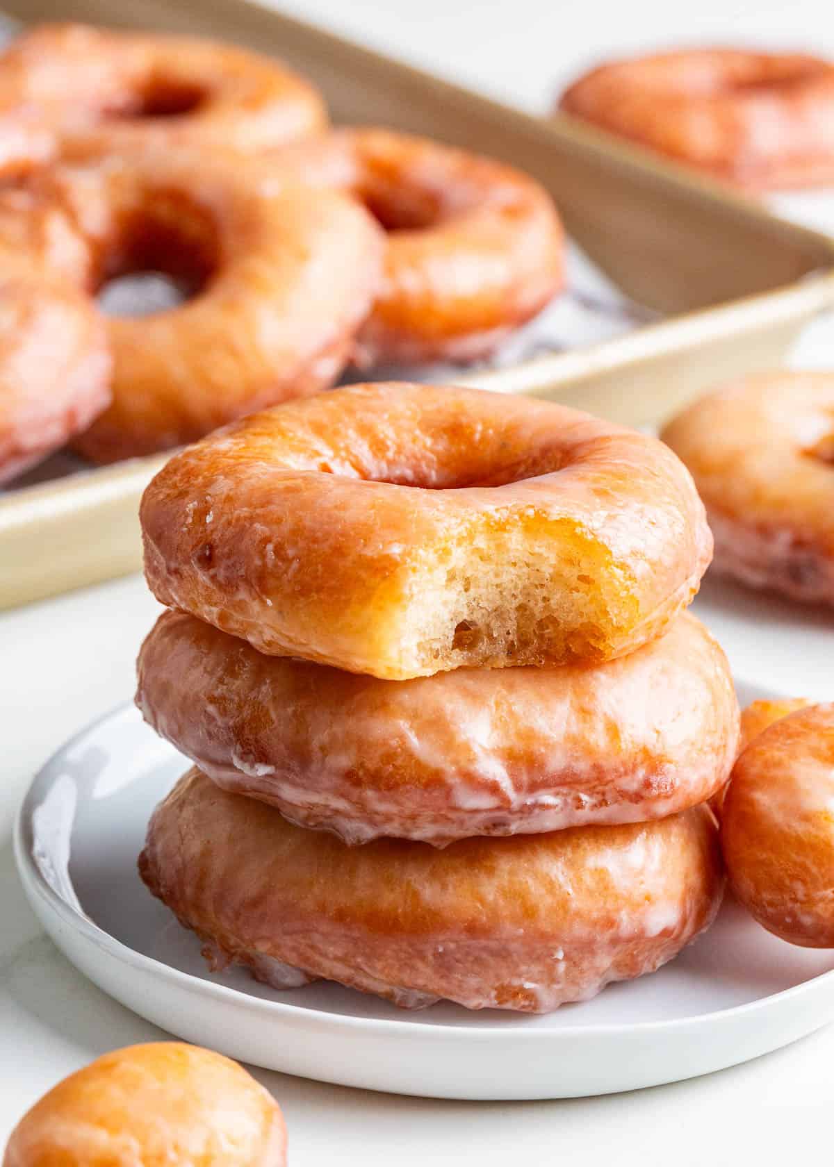 Learn to make easy homemade donuts that are light, airy, and infused with the flavors of vanilla and nutmeg. Dipped in a sweet vanilla glaze, these fried yeast donuts are the best! Stack of homemade donuts.