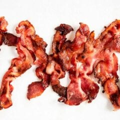 Crispy oven-baked bacon draining on a paper towel after cooking bacon in the oven.