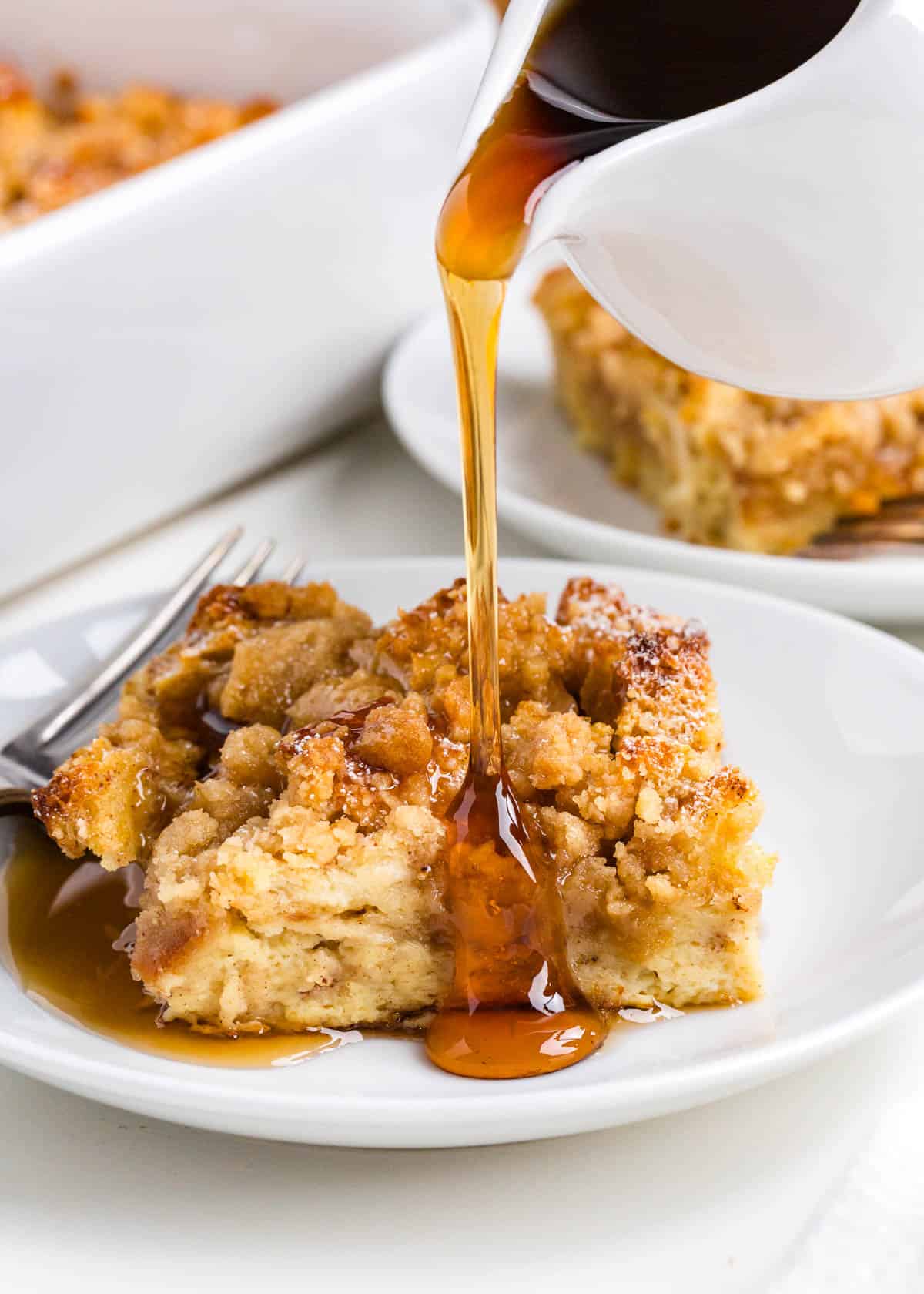 This French toast casserole has got everything French toast has, complete with a creamy custard and cinnamon crumb topping, but it's even easier to make! Pouring maple syrup over a slice of easy French toast casserole on a white plate
