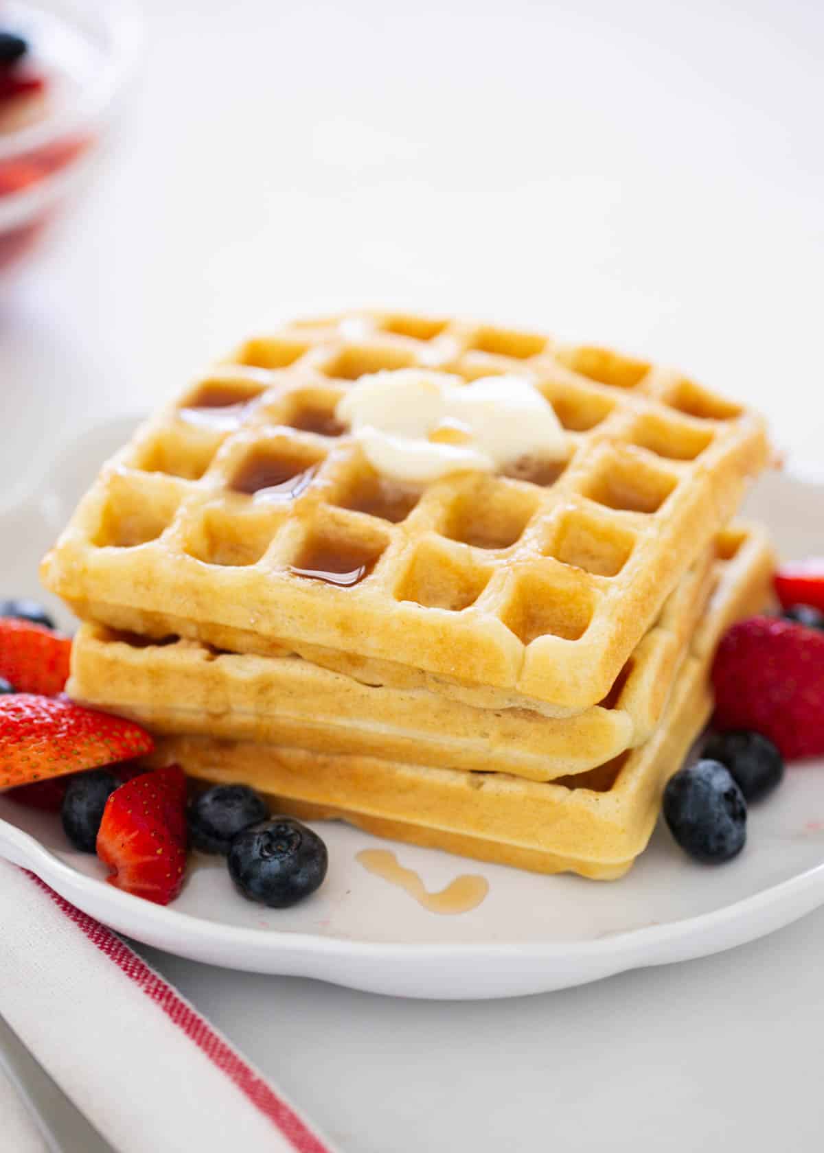 These buttermilk waffles are fluffy with the best crispy edges! This classic breakfast recipe makes mornings extra special when topped with fresh berries and maple syrup. Stack of buttermilk waffles.