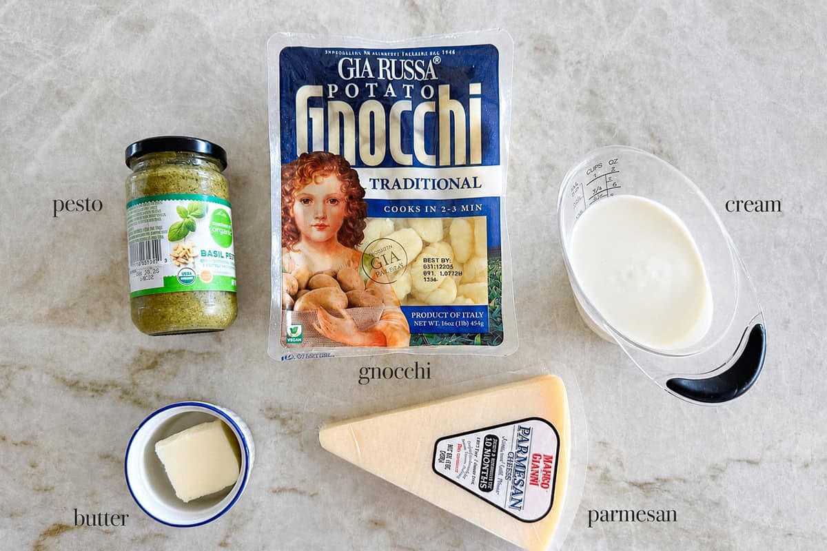 This 15-minute pesto gnocchi is easy to make with only 4 ingredients! Crispy, pillowy gnocchi is tossed with a creamy pesto sauce that will be a new favorite weeknight dinner. Pesto, gnocchi, cream, Parmesan and butter on the counter.