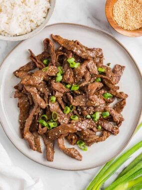 Cooked beef bulgogi garnished with sesame seeds and green onions on a serving plate.