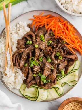 Bulgogi bowl recipe with marinated beef, steamed rice, shredded carrots, and sliced cucumber, finished with sesame seeds and green onions.