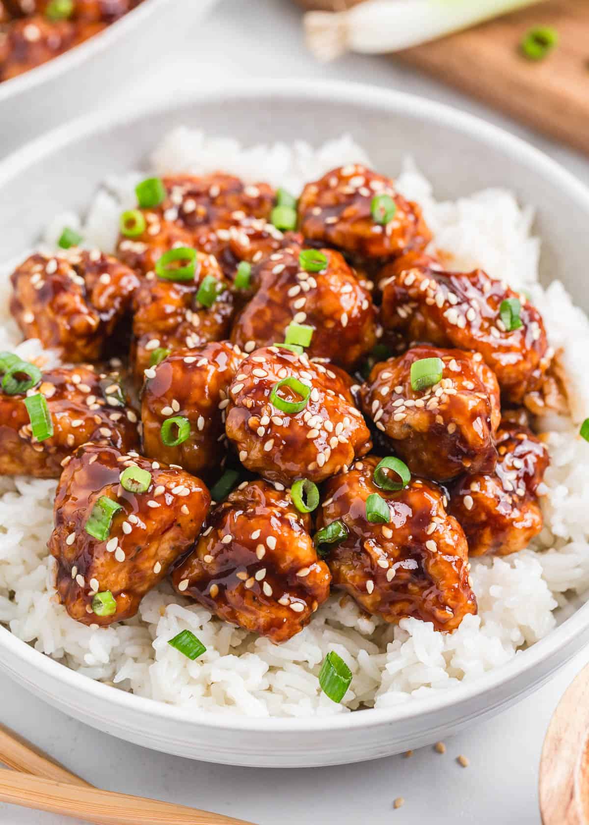 Little bites of crispy golden sesame chicken in a sweet and spicy sauce can be on your dinner table in under an hour, it's better than takeout. Serve with rice and veggies! Sesame chicken and rice in a bowl.