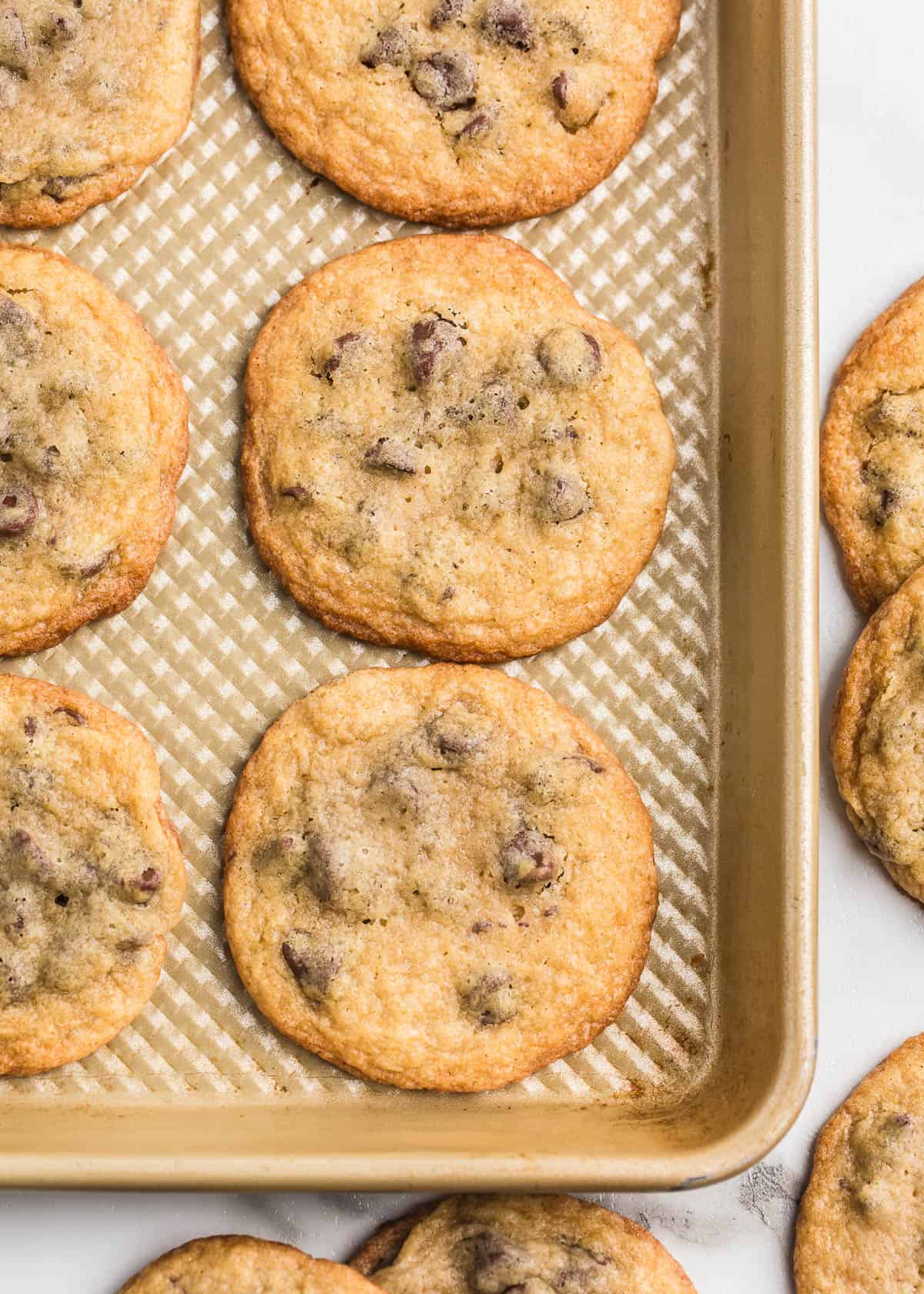 Bake up some nostalgia this weekend with this Toll House cookie recipe! They are thin, crispy cookies loaded with melty chocolate chips and a whole lot of good memories. Toll house cookies on a baking sheet showing crispy edges and melty chocolate chips.