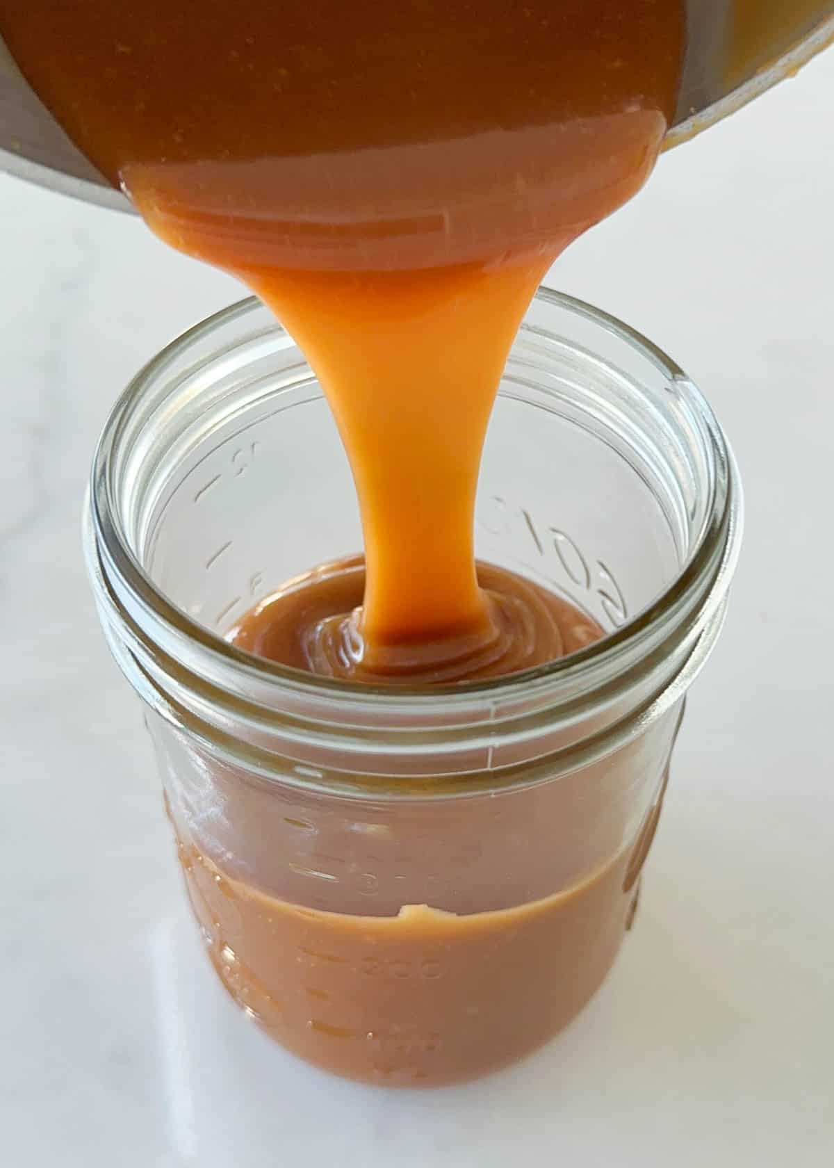 Never purchase store-bought again with this easy caramel sauce recipe! This no-fail, no-fuss homemade caramel really is the easiest to make with only 3 ingredients. Pouring easy caramel sauce into jar.