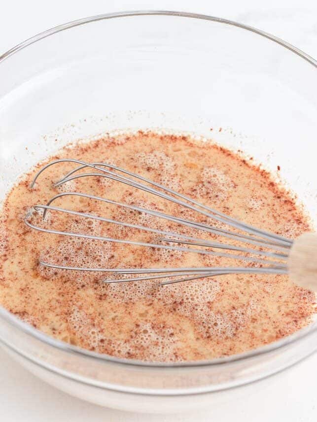 Milk and egg custard mixture in a glass bowl with whisk.
