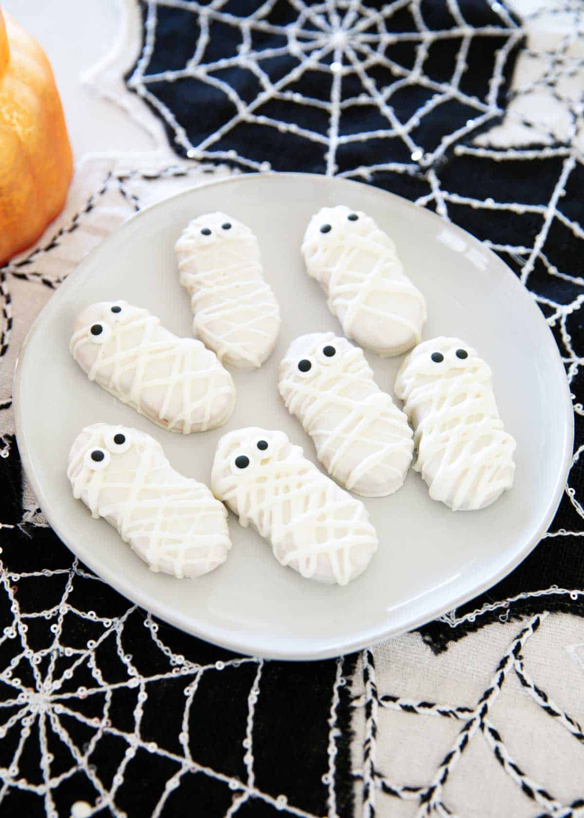 With only 3 ingredients, mummy cookies are a spooky Halloween treat that are super simple to make with Nutter Butter cookies, white chocolate and candy eyes. Mummy cookies on a plate.