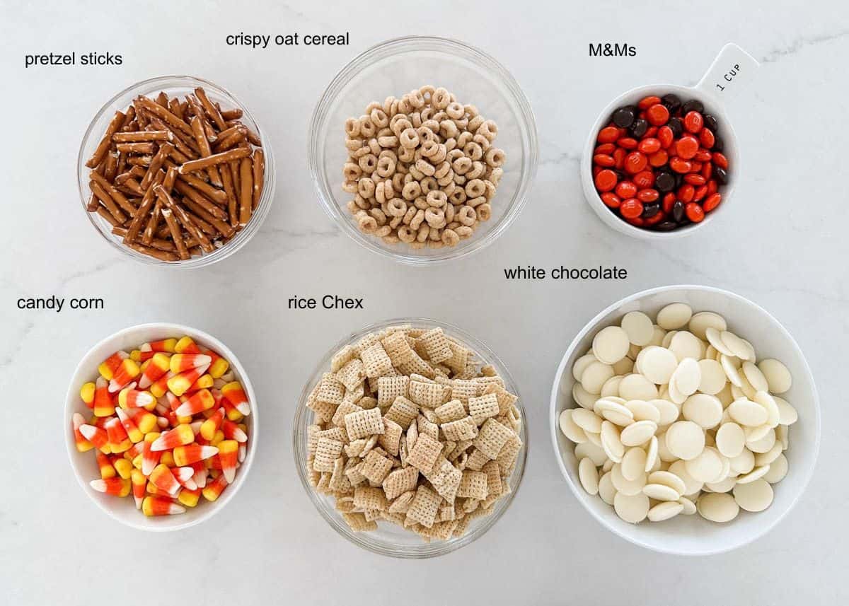 This Halloween Chex mix is sweet, crunchy and feeds a crowd! Everyone always loves this addicting monster munch with cereal, pretzels and candy coated in white chocolate. White chocolate Halloween chex mix ingredients on the counter.
