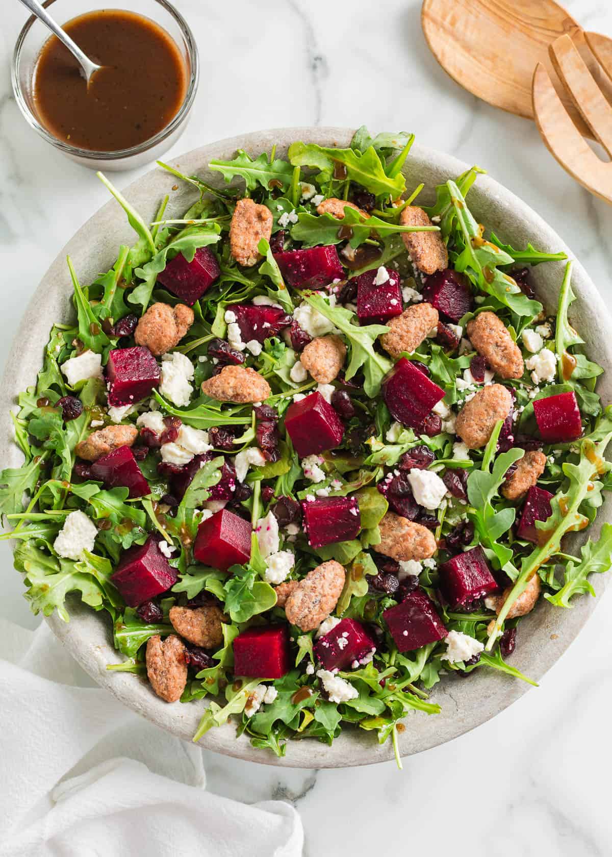 This beet salad is beautiful and bold with fresh arugula, crunchy candied pecans then tossed in a zesty balsamic dressing. It's stunning on any holiday table! Beet salad in a stone bowl.