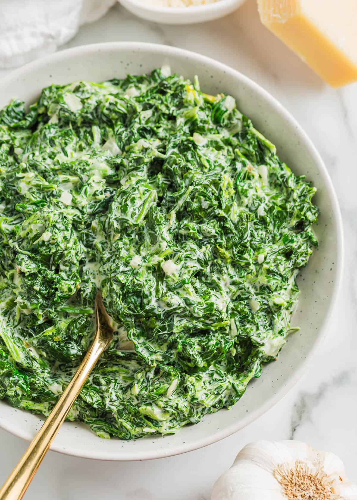 This creamed spinach is rich, flavorful and a quick and easy side dish made with frozen spinach and heavy cream. The silky white sauce pairs perfectly with the tender spinach! Creamed spinach in a white bowl.