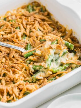 Close-up of Paula Deen&ndash;style green bean casserole in a white baking dish, topped with crispy French fried onions and creamy sauce.