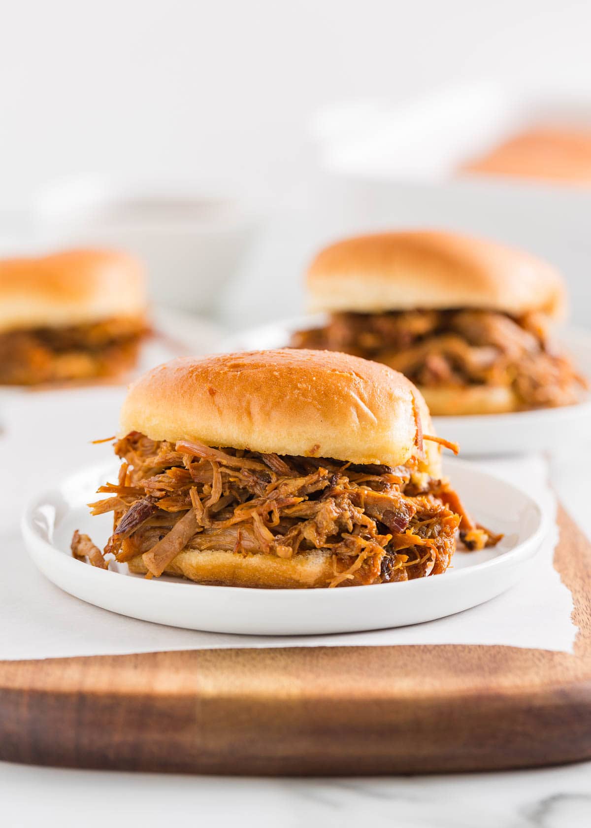 These pulled pork sliders are made with slow-cooked shredded pork smothered in a sweet, savory, and smoky BBQ sauce piled high on Hawaiian buns! Pork sliders on a white plate.