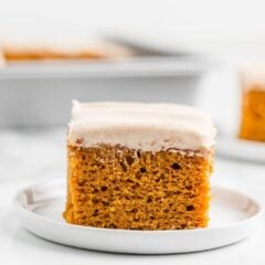 Slice of moist pumpkin cake topped with spiced cream cheese frosting on a white plate.