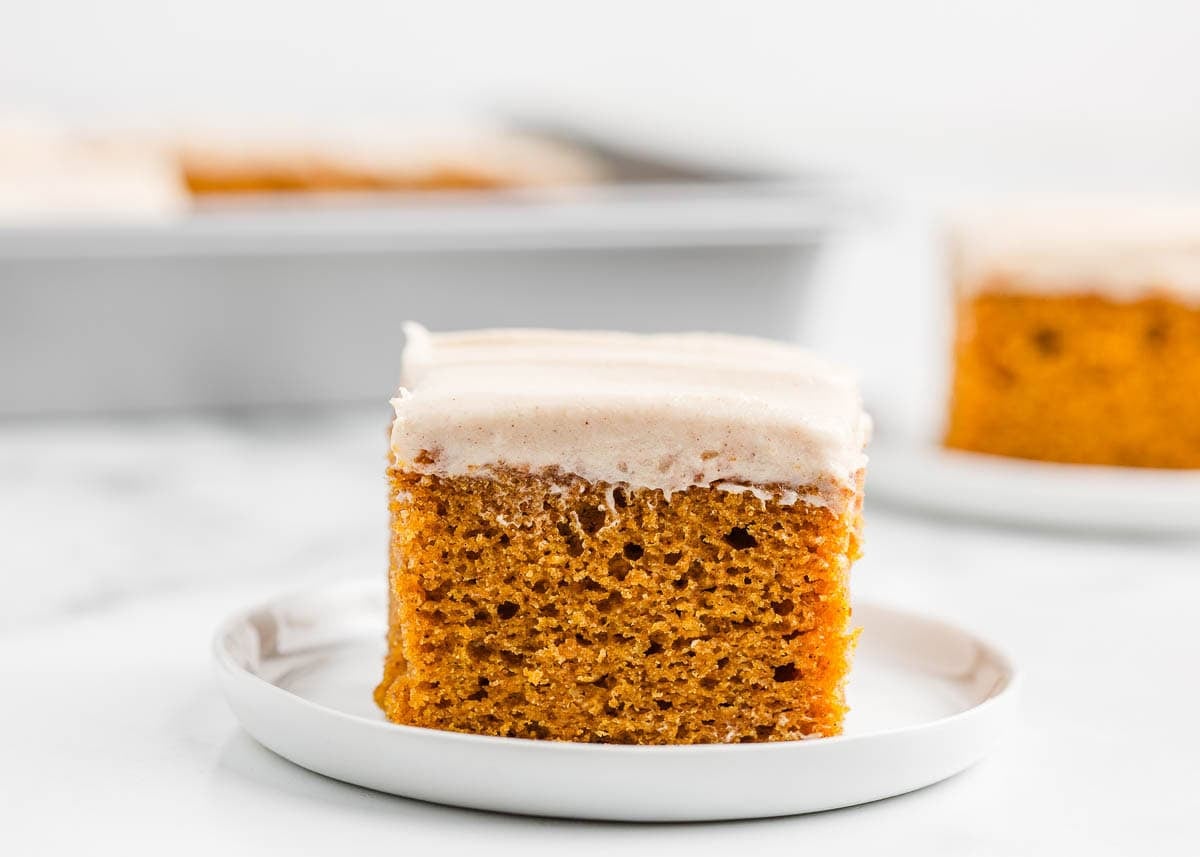 Slice of moist pumpkin cake topped with spiced cream cheese frosting on a white plate.