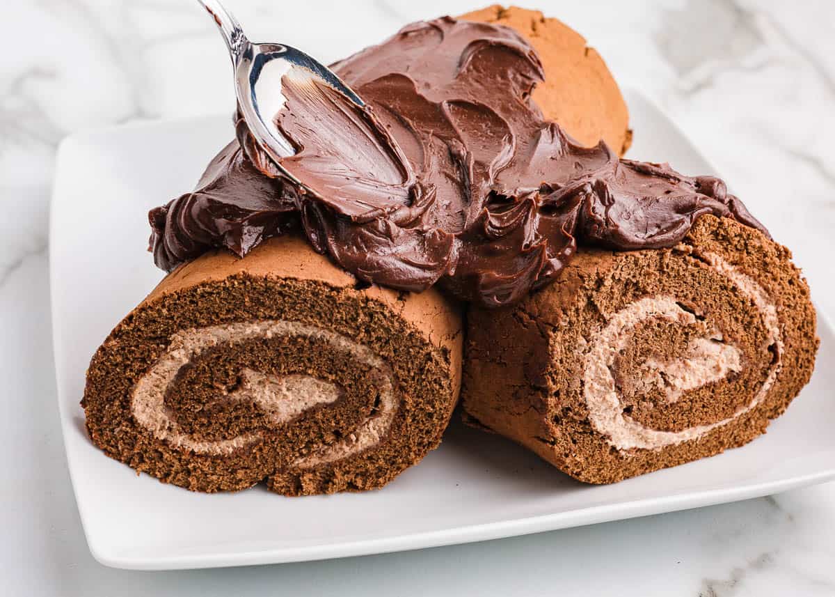 This Christmas make a traditional yule log cake (bûche de noël). A chocolate sponge cake is filled with creamy mascarpone, then covered with chocolate ganache for the bark. Spreading frosting on yule log cake.