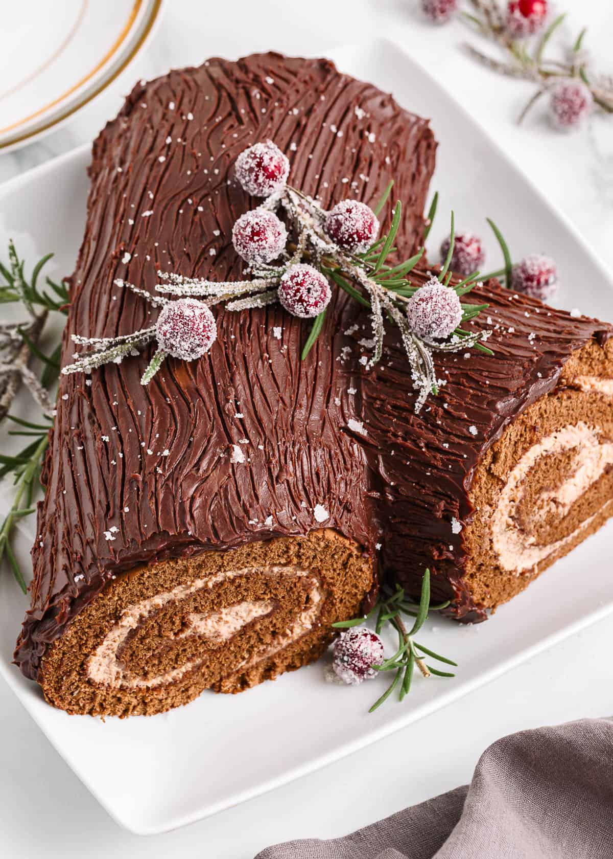 This Christmas make a traditional yule log cake (bûche de noël). A chocolate sponge cake is filled with creamy mascarpone, then covered with chocolate ganache for the bark. Yule log cake with cranberries on top.