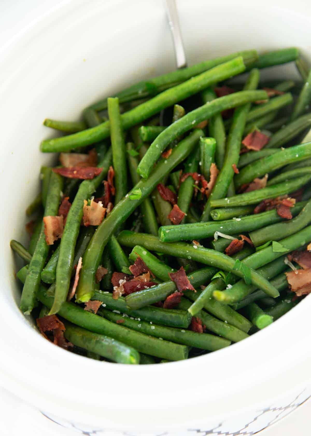 These crockpot green beans are a simple side dish made with fresh green beans, onion and smokey bacon! This easy recipe made in the slow cooker will be your new favorite. Crockpot green beans.