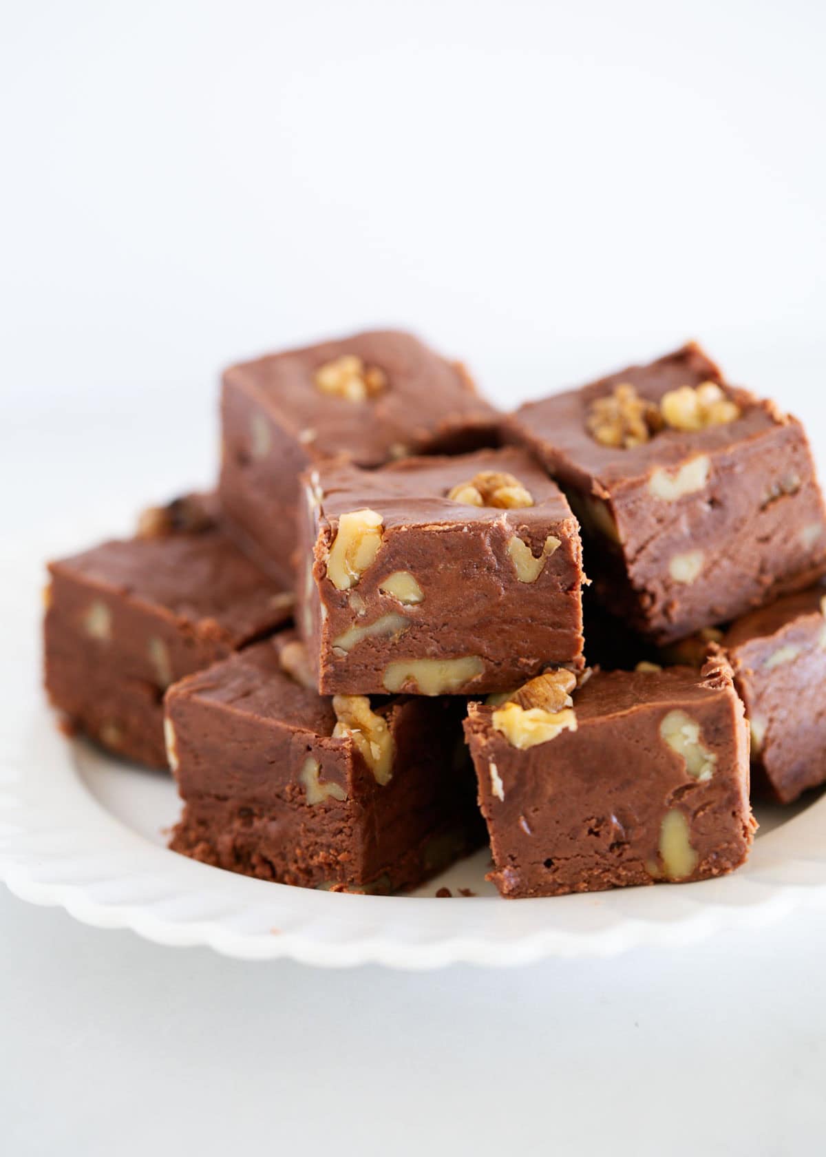 Just like the original recipe from the back of the Kraft marshmallow creme jar, fantasy fudge is a classic holiday treat for Christmas made with chocolate chips and walnuts! A plate of stacked fantasy fudge.