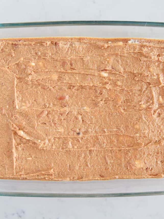 Refried beans spread into a baking dish.