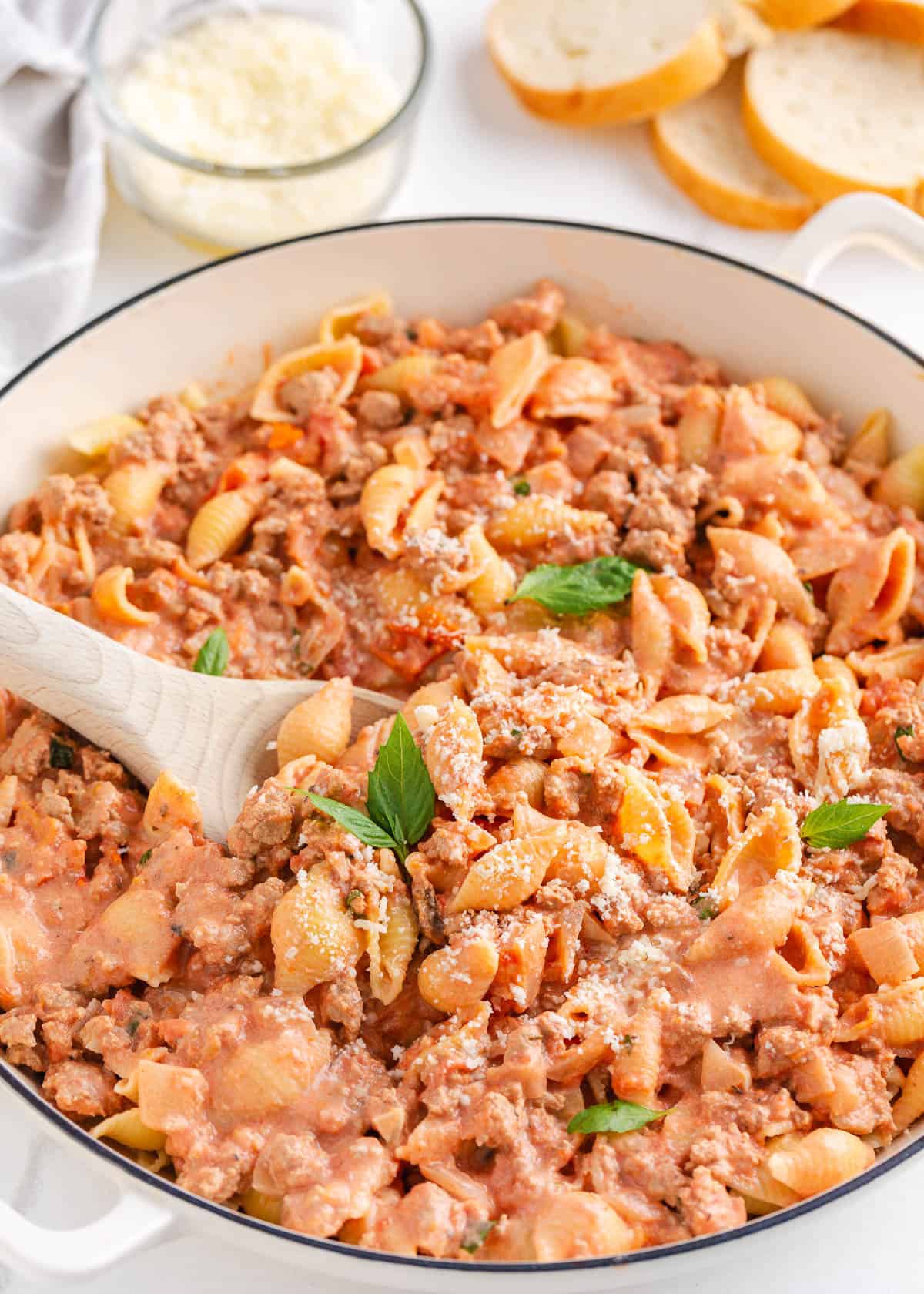 This ground turkey pasta dish is made with small shell noodles and seasoned ground turkey tossed in a rich, tomato cream sauce and garnished with fresh herbs! Ground turkey pasta in a large white skillet with serving spoon.