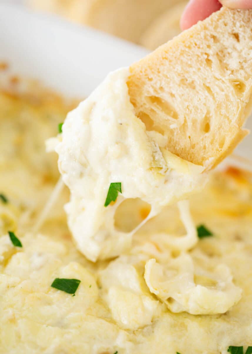 Dipping bread in artichoke dip.