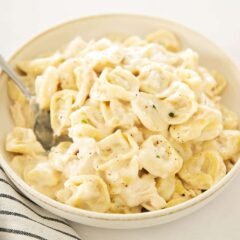 Bowl of creamy chicken tortellini Alfredo topped with black pepper.