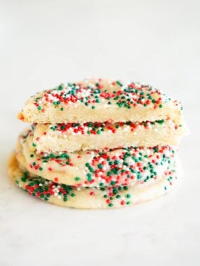 Stack of soft drop sugar cookies coated in red, green, and white sprinkles, with the top cookie broken in half to show the tender, chewy center.