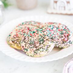 Drop sugar cookies with festive sprinkles on a plate with holiday decor in background.