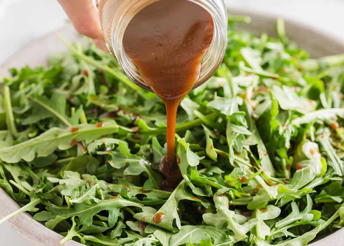 Pouring balsamic dressing over arugula before adding beets and tossing the salad together.