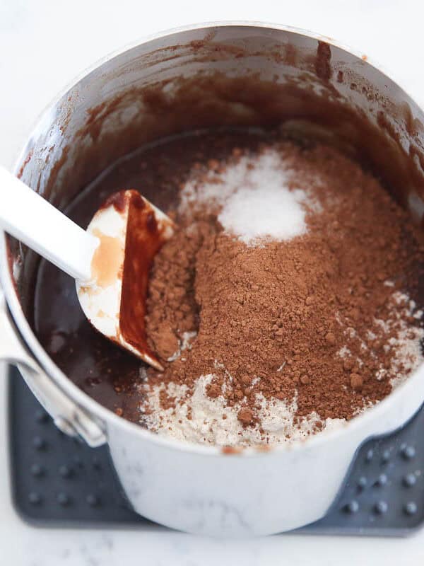 Flour and cocoa powder added to melted chocolate in a saucepan.