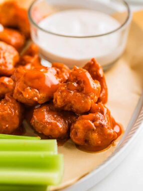 Fried boneless chicken wings on a serving plate with dip and celery.