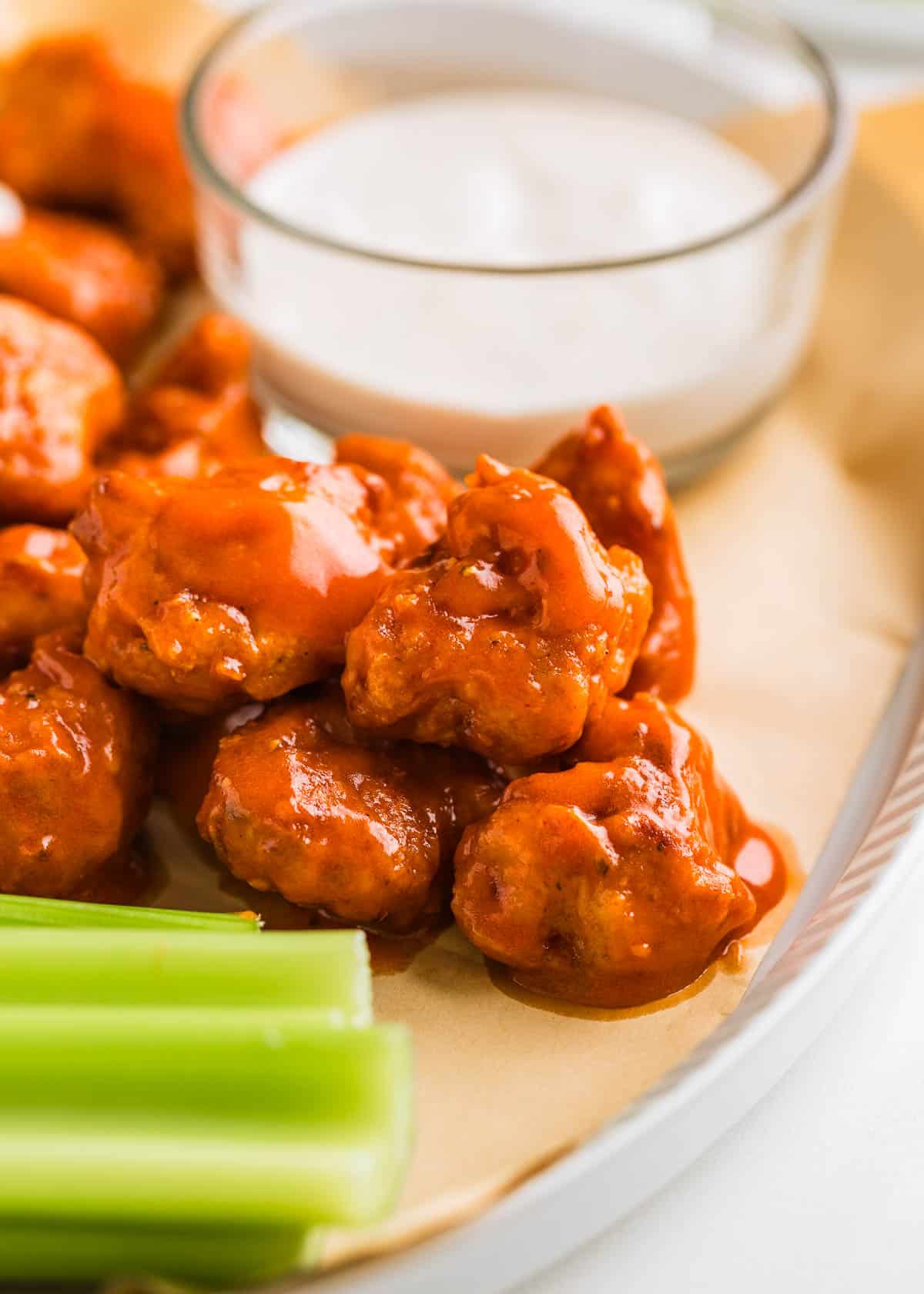 These boneless chicken wings are made with cubes of tender chicken breast coated in the crispiest buttermilk batter, fried to perfection then tossed in 2 different sauces! Boneless chicken wings on a serving plate with dip and celery.