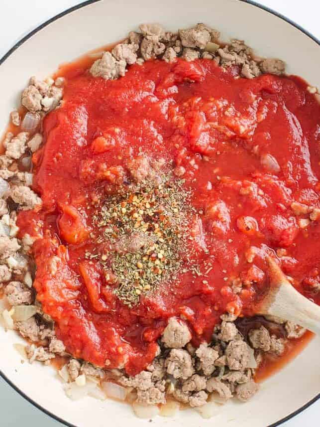 Ground beef with tomato sauce and seasonings in a skillet.