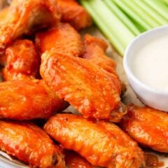 Crispy baked buffalo chicken wings on a serving platter with ranch dressing and celery.