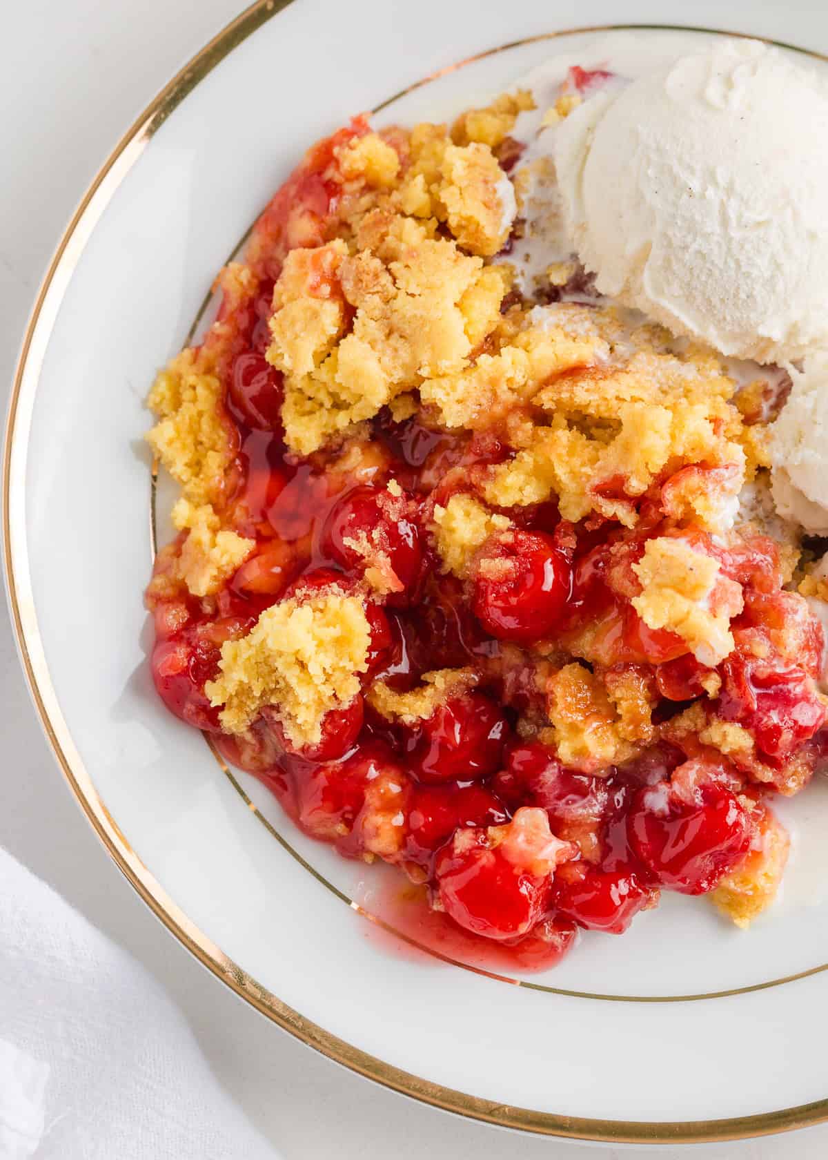 Make the easiest cherry dump cake with a boxed cake mix and canned cherry pie filling. Dump everything into a dish and bake it until it's golden on top and bubbly on the bottom! Cherry dump cake on a white plate.