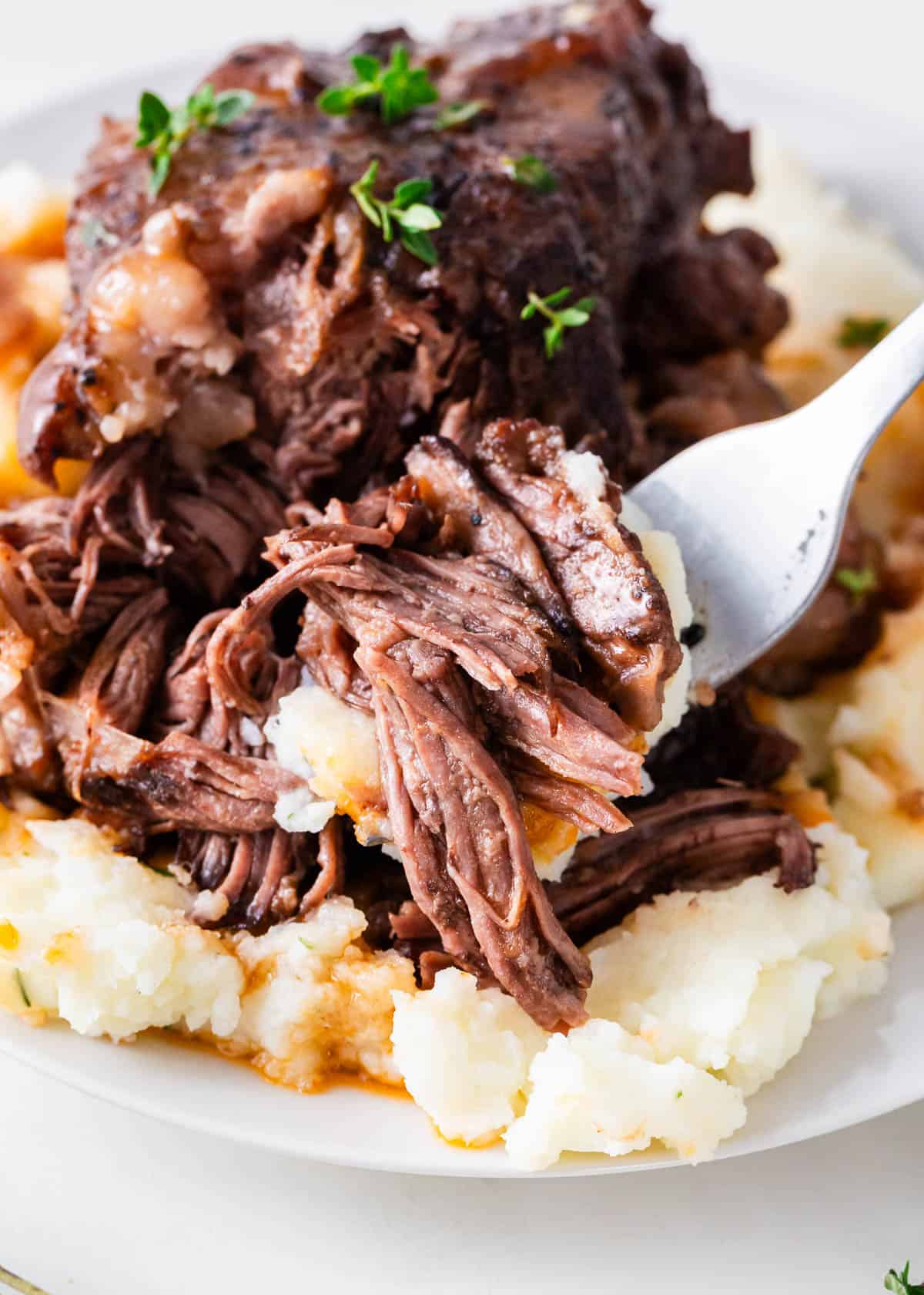 These red wine braised beef short ribs cook low and slow in a Dutch oven with red wine and beef stock until succulent and fall-off-the-bone tender. Serve over mashed potatoes for pure comfort! A forkful of braised short ribs over mashed potatoes.