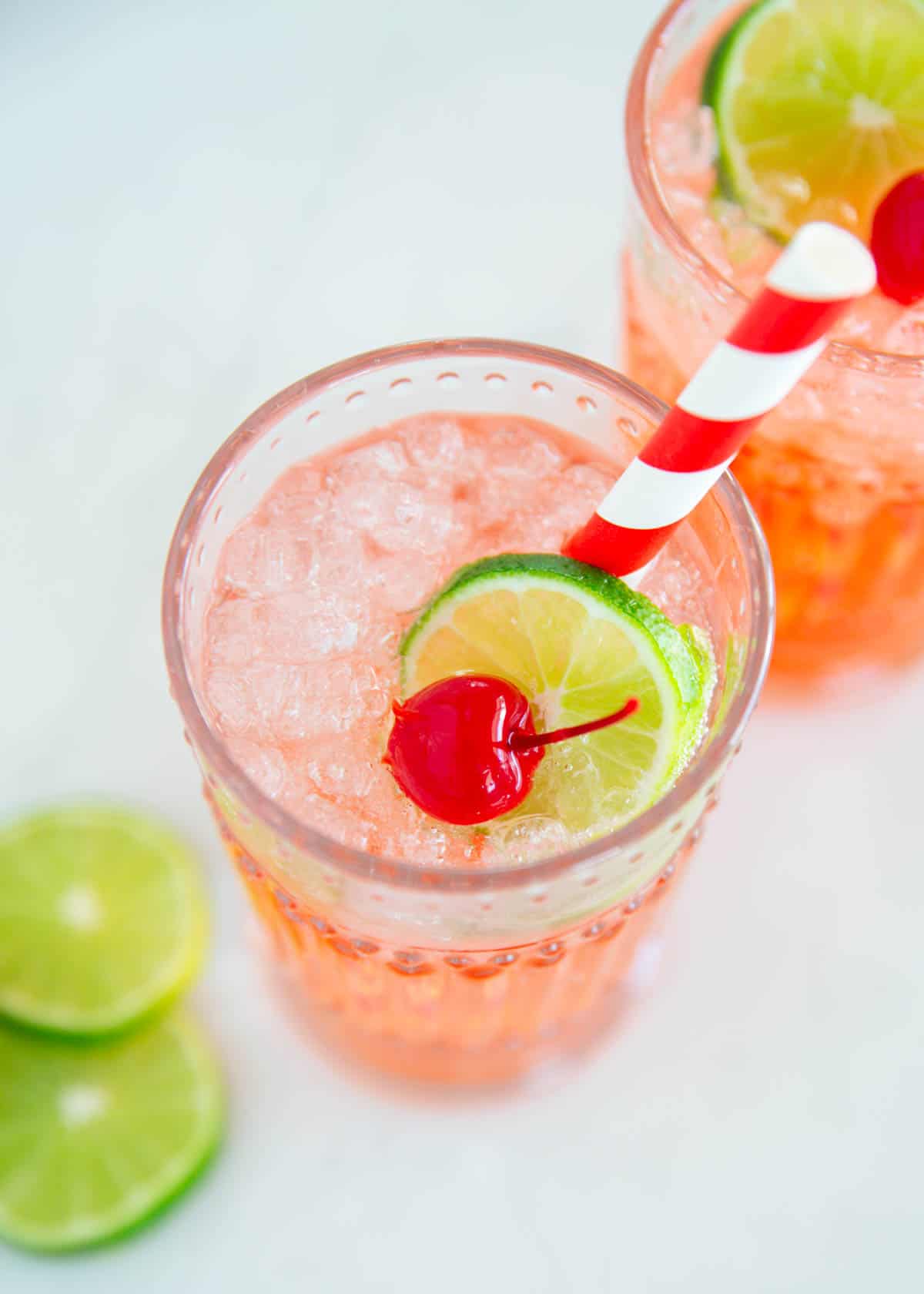This copycat recipe for Sonic cherry limeade is easy to make with 7Up lemon lime soda, maraschino cherries and a lime wedge. This family friendly drink is a sweet treat! Cherry limeade in a glass cup.