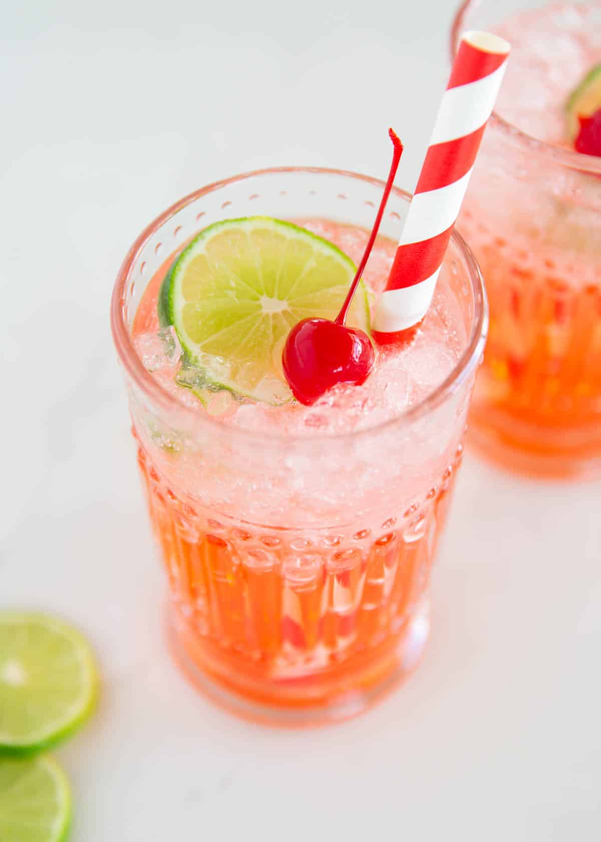 This copycat recipe for Sonic cherry limeade is easy to make with 7Up lemon lime soda, maraschino cherries and a lime wedge. This family friendly drink is a sweet treat! Cherry limeade in a glass cup.