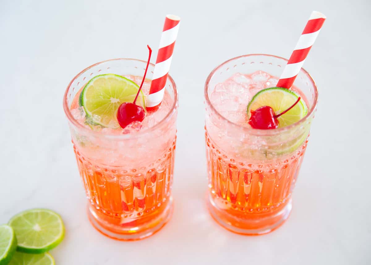 This copycat recipe for Sonic cherry limeade is easy to make with 7Up lemon lime soda, maraschino cherries and a lime wedge. This family friendly drink is a sweet treat! Two glasses of cherry limeade.