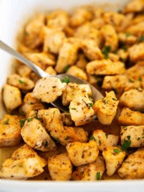 Baked chicken bites in baking dish with serving spoon.