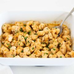 Oven baked chicken bites in baking dish with serving spoon.